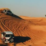 Two SUVs driving through the sand dunes during a desert adventure tour in Dubai.